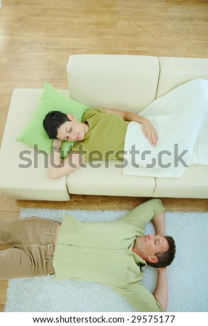 Couple sleeping at home on sofa and on floor. Overhead view.