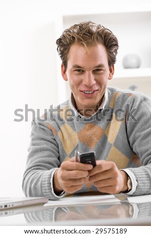 Happy young man using mobile phone at home, smiling.