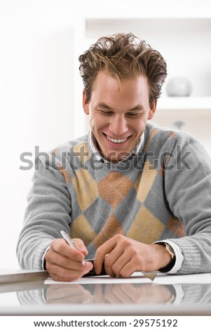 Happy young man writing on desk at home, smiling.