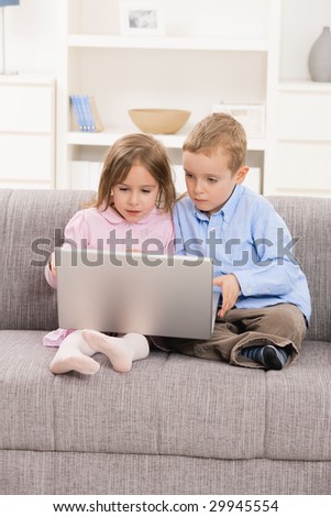 Young children sitting on couch at home, using laptop computer, looking at screen.