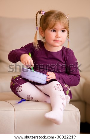 Little girl in purples dress, playing with plastic toy dishes, sitting on couch at home.