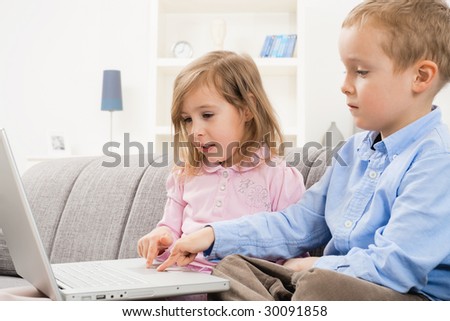 Young siblings sitting on couch at home, browsing internet on laptop computer, looking at screen.