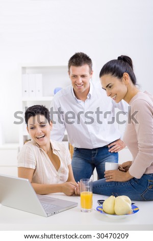 Happy, smiling office workers sitting at desk, looking at laptop computer screen.