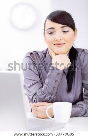 Young businessman sitting at desk at office, thinking, smiling.