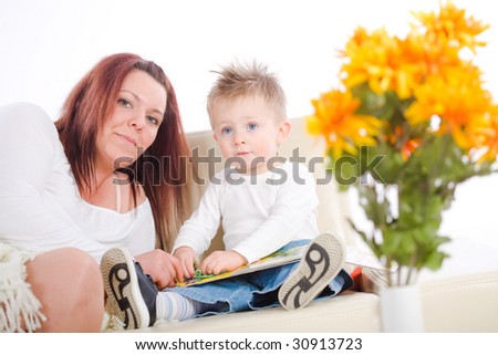 Happy family sitting on sofa at home mother reading for baby boy from story book.