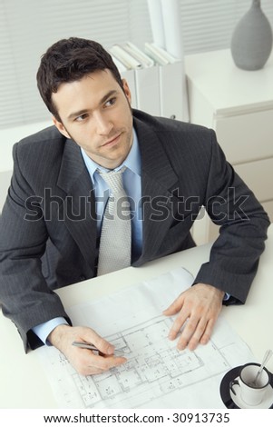 Young businessman, sitting at office desk, planning office layout. Overhead shot.