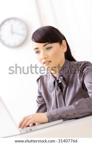 Businesswoman working hard on her laptop computer in brightly lit office.
