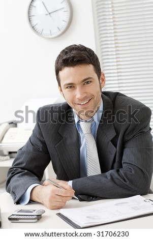 Happy young businessman working at desk at office, smiling.
