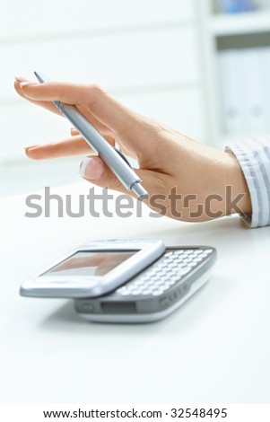 Closeup picture of female hand holding pen, using smart mobile phone.