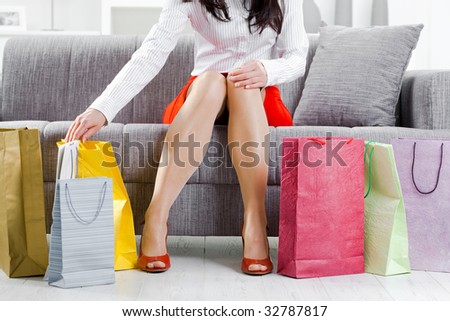 Young woman sitting on couch after day of shopping, packing colorful shopping bags.