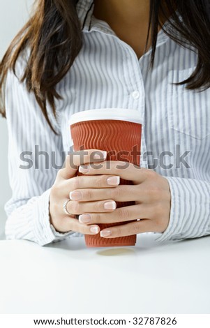 Closeup of female hands holding a red mug. Selective focus on hands and fingers.