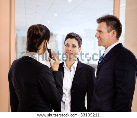 Business team standing in office hallway, businesswoman talking on mobile phone.