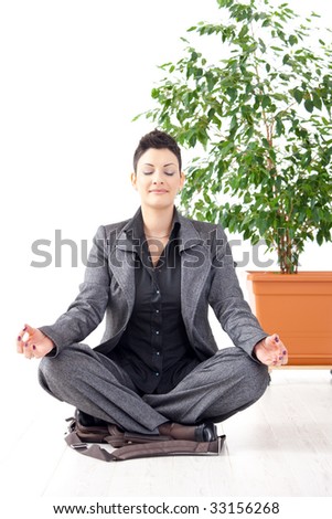 Young businesswoman sitting in yoga lotus position, holding laptop computer, meditating with closed eyes.