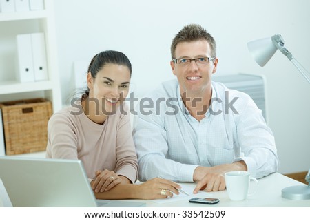 Happy young casual couple sitting  at desk working together at home office, smiling.