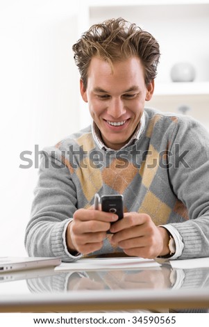 Happy young man using mobile phone at home, smiling.