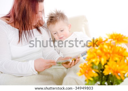 Happy family sitting on sofa at home mother reading for baby boy from story book.