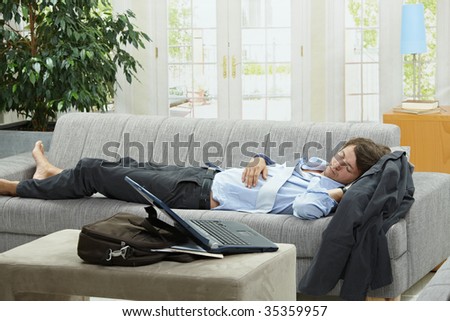 Tired businessman sleeping on couch at home after long day of work.