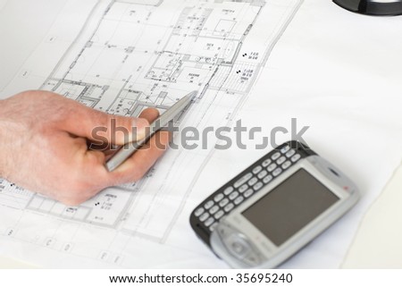 Architect's hand pointing with pen to flooor plan on desk with mobile phone on it.