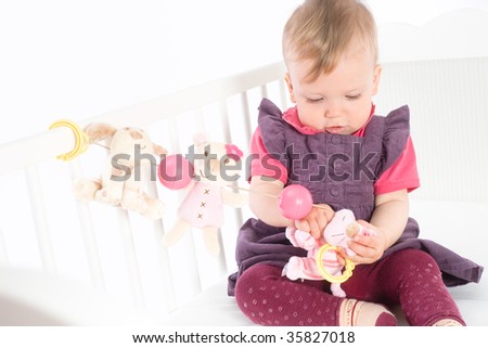 Cute baby girl (1 year old) sitting on crib, holding soft toys. Isolated on white, smiling. Toys are offically property released.