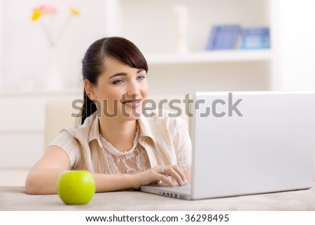 Happy young women browsing internet on laptop computer at home, smiling.