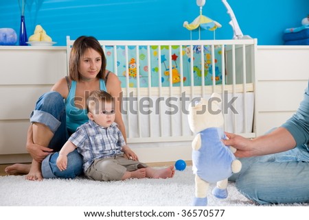 Portrait of happy family at home. Baby boy ( 1 year old ) and young parents father and mother sitting on floor and playing together at children\'s room, smiling.
