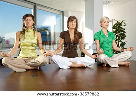 Young businesswomen sitting in yoga position on meeting room table.