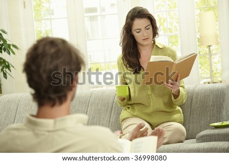 Young  couple reading book sitting at home on couch. Selective focus on women.
