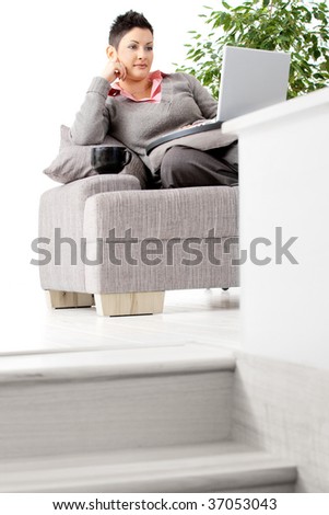 Young woman sitting on couch working on laptop computer at home.