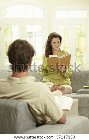 Young  couple reading book sitting at home on couch. Selective focus on women.