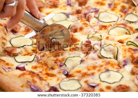 Humand hand cutting pizza slices with pizza cutter.