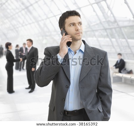 Young businessman talking on mobile standing in office hallway.