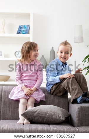 Portrait of happy little brother and sister sitting together on couch, smiling.