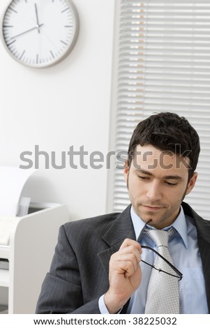 Portrait of young businessman thinking, holding his glasses, looking down.