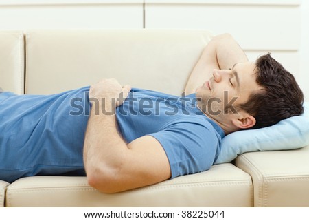 Young handsome man sleeping on couch at home, side view.