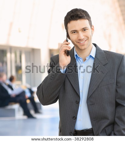 Portrait of happy businessman talking on mobile in office hallway.