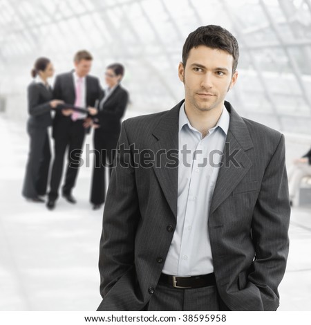 Portrait of seriouis businessman standing in office hallway with hands in pocket.