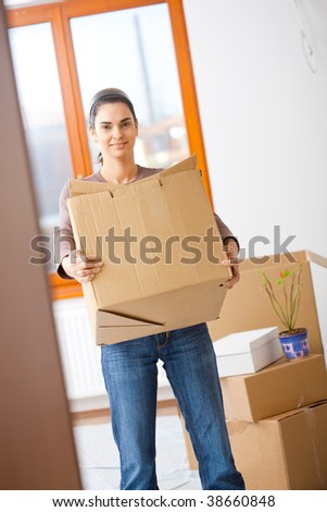 Woman lifting cardboard box while moving home, smiling.
