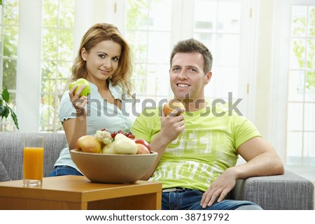 Love couple having breakfast together, holding apples, looking at camera smiling.