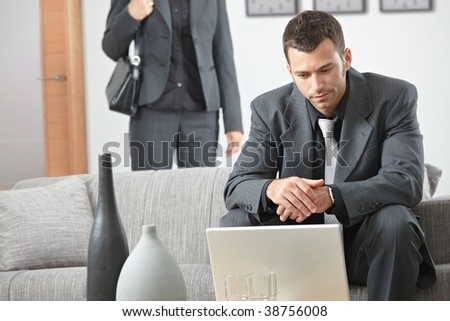 Young businessman sitting on sofa at office, working with laptop computer.
