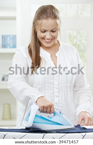 Happy young woman ironing on ironing board at home, smiling.
