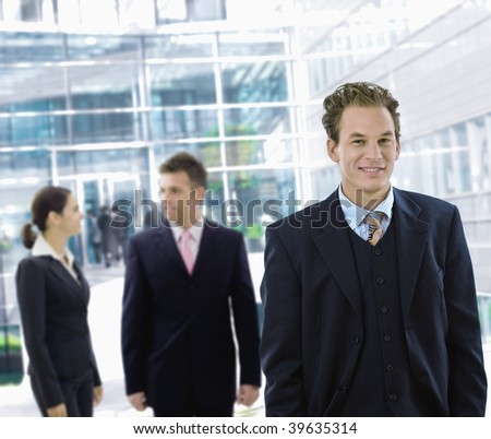Businessman leaving office building aong other businesspeople in the background.