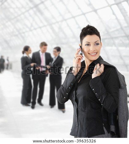 Portrait of happy businesswoman talking on mobile phone on office hallway.