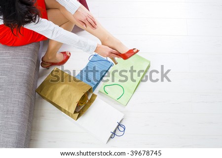 Young woman sitting on couch taking off shoes,  colorful shopping on the floor.