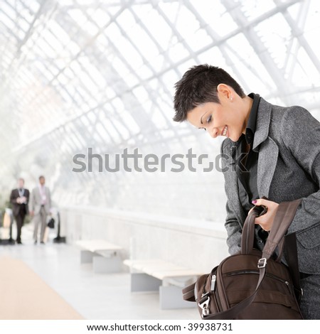 Businesswoman standing in office hallway, searching something in laptop bag, looking down.