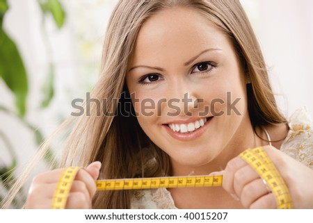Happy young woman on diet holding tape measure, smiling.