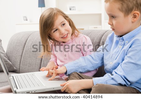 Happy children sitting on couch at home, browsing internet on laptop computer. Girl smiling at boy who focusing at screen.