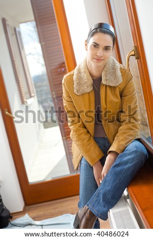 Portrait of attractive young woman sitting at window, smiling.