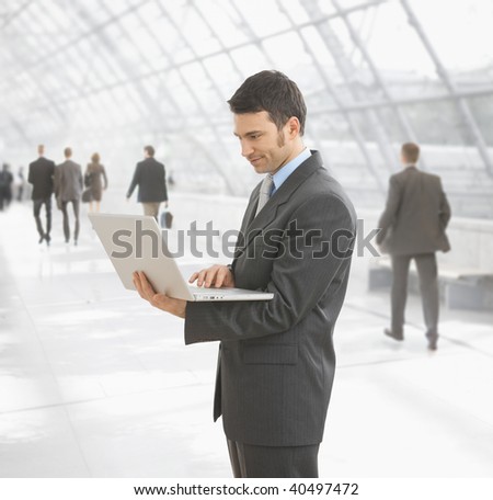 Businessman using laptop computer standing on office hallway.