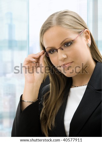 Young businesswoman standing with arms crossed in front of office windows, smiling.