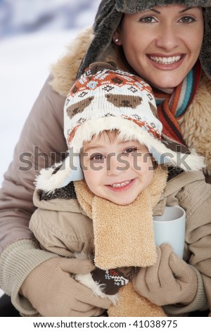 Portrait of happy mother and child holding cup of hot tea in snow on a cold winter day laughing, smiling.